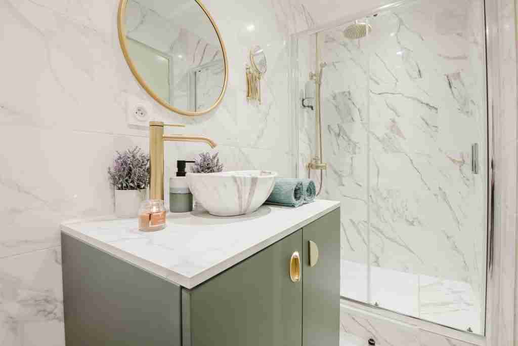 Salle de bain moderne avec douche vitrée et élégante vasque sur meuble vert. Décoration en marbre et métaux dorés ajoutant une touche luxueuse et contemporaine.